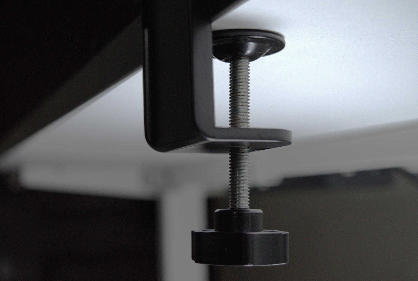 Black power strip holder mounted to the white desk with C-Clamp