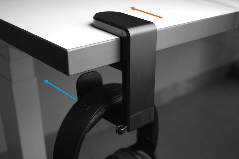 Black headphone hanger clamped to the front side of a white desk